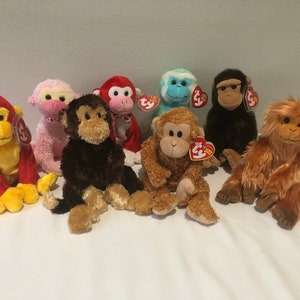 May include: A collection of plush monkey toys in various colors, including red, pink, brown, and blue. Each monkey has a unique expression and features a Ty tag. The monkeys are sitting on a white surface.