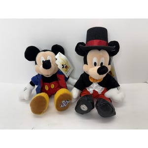 Peut inclure: Deux peluches Mickey Mouse. L'un porte une veste bleue, un short rouge et des chaussures jaunes avec "30" sur une chaussure. L'autre Mickey porte un smoking noir, un pantalon rouge et un haut-de-forme noir avec une bande rouge. Les deux ont des &eacute;tiquettes.