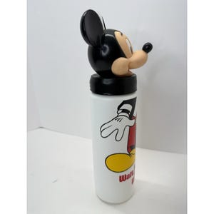 May include: White water bottle featuring a Mickey Mouse design. The bottle has a black lid and a black and tan Mickey Mouse head on top. The bottle has a cartoon graphic of Mickey Mouse and the words "Walt Disney World" in red.
