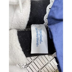 May include: Close-up of a plush toy with a white collar and a black bodice. A tag with the text "Disneyland Walt Disney World" is visible. The toy has blue fabric and white lace trim.