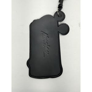 May include: Black leather luggage tag with the embossed word "Mondani". The tag has a unique shape with rounded edges and a small loop at the top for attachment. A black strap and clasp are attached.