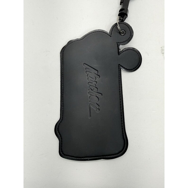 May include: Black leather luggage tag with the embossed word "Mondani". The tag has a unique shape with rounded edges and a small loop at the top for attachment. A black strap and clasp are attached.