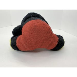 May include: A plush toy in the shape of a cartoon character, featuring a black head and limbs, and a large red body. The toy has yellow accents on the feet.