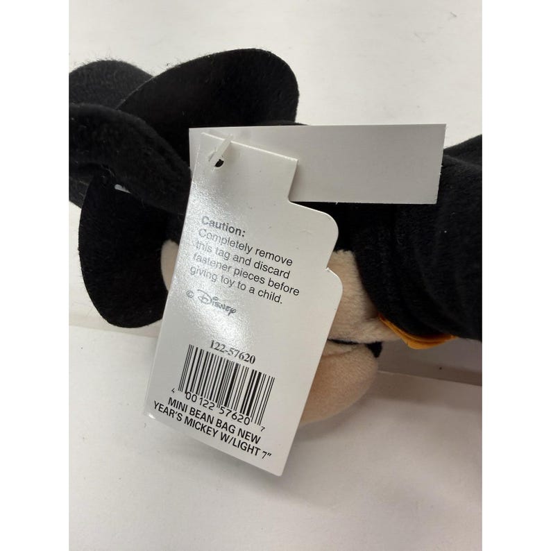 Peut inclure: Un petit jouet en forme de Mickey Mouse en sac de haricots avec un chapeau et des oreilles noirs. Le jouet porte une &eacute;tiquette avec le texte "MINI BEAN BAG NEW YEAR'S MICKEY W/LIGHT 7" et un avertissement.