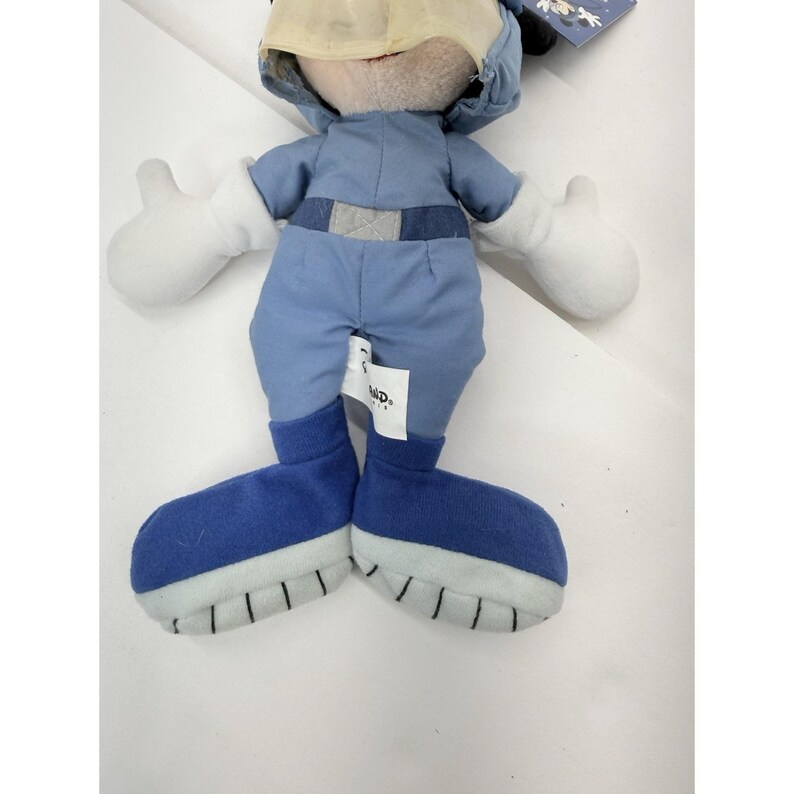 May include: A plush toy of a cartoon character wearing a blue outfit with a matching hat and boots. The character has white gloves and a tan face. The toy has a tag attached.