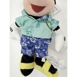 May include: A Mickey Mouse plush toy wearing a light blue shirt with a floral pattern and blue shorts with white flowers. The toy has black shoes with yellow stripes and white gloves. A Disney Store tag is attached.