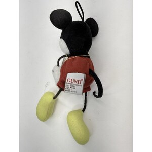 K&ouml;nnte beinhalten: Ein Pl&uuml;schtier von Mickey Mouse mit schwarzen Ohren, einem schwarzen Kopf, einem wei&szlig;en Gesicht, roten Shorts und gelben F&uuml;&szlig;en. Das Spielzeug hat eine schwarze Schlaufe zum Aufh&auml;ngen und ein wei&szlig;es Etikett mit der Marke "GUND".