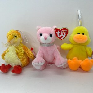 May include: Three plush toys: a yellow chick with red feet, a pink cat with a silver collar, and a yellow duck with orange feet. The toys are all Ty Beanie Babies.