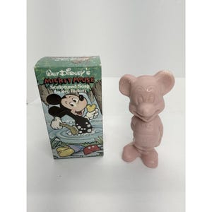 May include: A pink Mickey Mouse sculpted soap figure stands next to its box. The box features a cartoon Mickey Mouse illustration and the text "Walt Disney's Mickey Mouse Sculpted Soap by Ben Rickert". The soap is a light pink color.