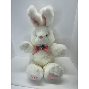 May include: A plush white bunny with long ears, pink inner ears, and a pink nose. It has a pink bow with a purple flower accent and pink accents on its feet. The year "2000" is printed on one foot.