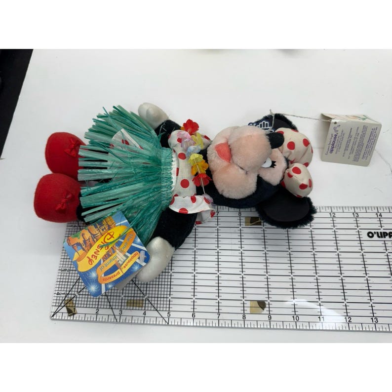 Puede incluir: Una mu&ntilde;eca de peluche de Minnie Mouse con falda hawaiana, collar de flores y lazo de lunares rojos. La mu&ntilde;eca tiene zapatos rojos y una etiqueta que dice "Disney".