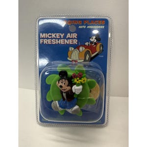 May include: Mickey Mouse air freshener in a plastic package. The air freshener features Mickey Mouse holding flowers, with a green background. The packaging reads "Going Places Auto Accessories" and "Mickey Air Freshener".