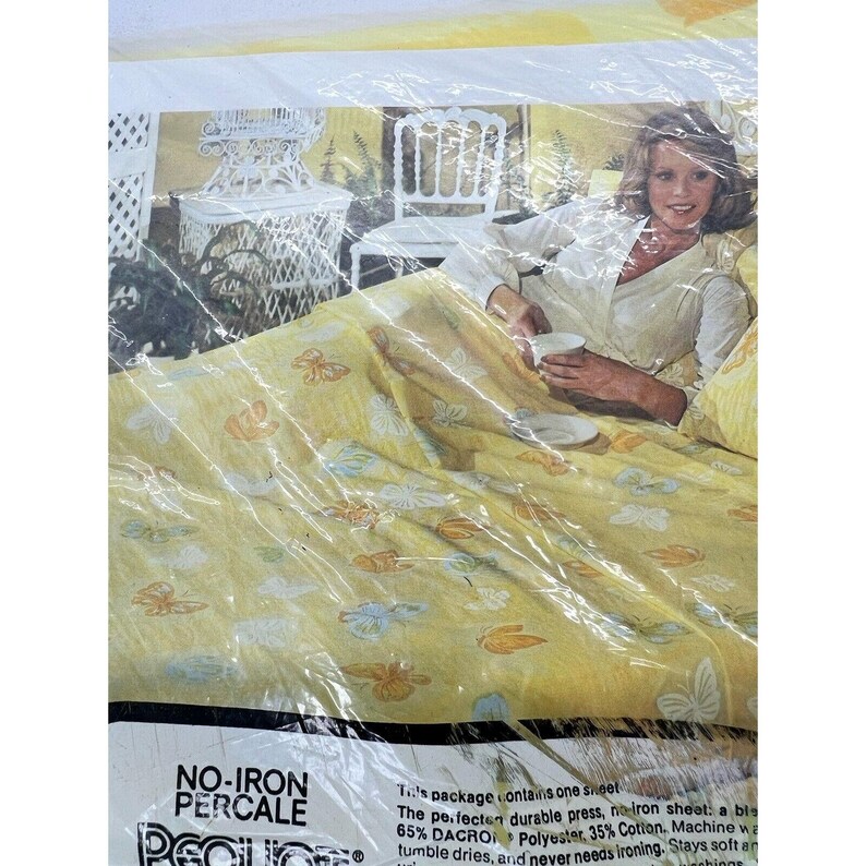 May include: A yellow and white no-iron percale sheet with a butterfly print. The package contains one sheet, 65% Dacron Polyester and 35% Cotton. Machine washable and tumble dry. The sheet is shown on a bed with a woman sitting on it holding a cup.
