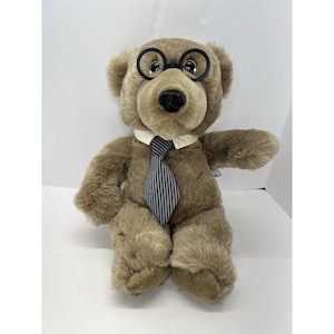 May include: A brown teddy bear wearing round black glasses and a striped blue and white tie. The bear is sitting with its paws in front of it.