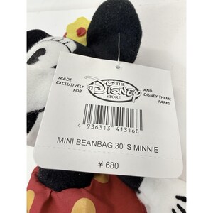 Puede incluir: Un peluche mini beanbag de Minnie Mouse. El peluche tiene orejas negras, una cara blanca y un vestido de lunares rojos y blancos. La etiqueta dice "MINI BEANBAG 30' S MINNIE" y "THE DISNEY STORE".
