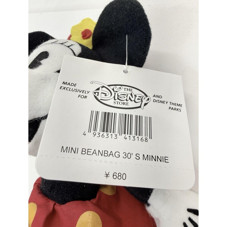 Puede incluir: Un peluche mini beanbag de Minnie Mouse. El peluche tiene orejas negras, una cara blanca y un vestido de lunares rojos y blancos. La etiqueta dice "MINI BEANBAG 30' S MINNIE" y "THE DISNEY STORE".