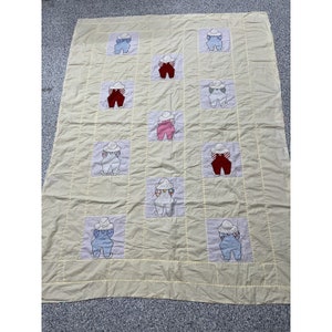 May include: A vintage quilt with a yellow background and a repeating pattern of embroidered figures wearing overalls and hats. The figures are in various colors, including blue, red, and pink.