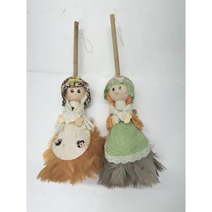 May include: Two handmade doll dusters. Each doll has a fabric head, a wooden handle, and a skirt made of feathers. One doll has a brown feather skirt, and the other has a gray feather skirt. The dolls have fabric bonnets and aprons.