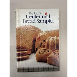 May include: A cookbook titled "The Red Star Centennial Bread Sampler" featuring images of various breads, including sliced loaves, rolls, and cinnamon rolls. The cover has a white background with the title in blue and a red star.