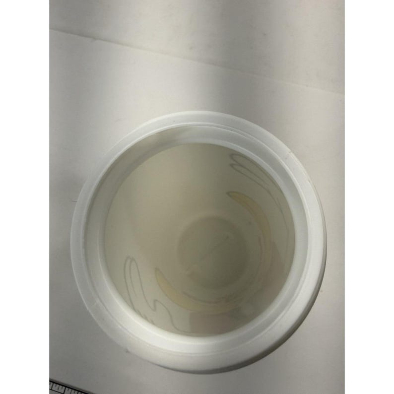 May include: An overhead view of a white plastic container with a wide rim. The interior of the container is off-white with a faint floral design. The container is sitting on a white surface.