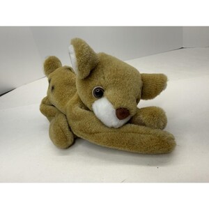May include: A plush toy in the shape of a brown bear with a white muzzle and inner ears. The bear has large, black eyes and a brown nose. The toy is lying down, with its paws crossed.