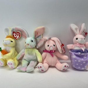 May include: Four plush bunny toys, each with a different colour and design. The bunnies are all wearing Ty Beanie Babies tags. The bunnies are sitting on a white surface.
