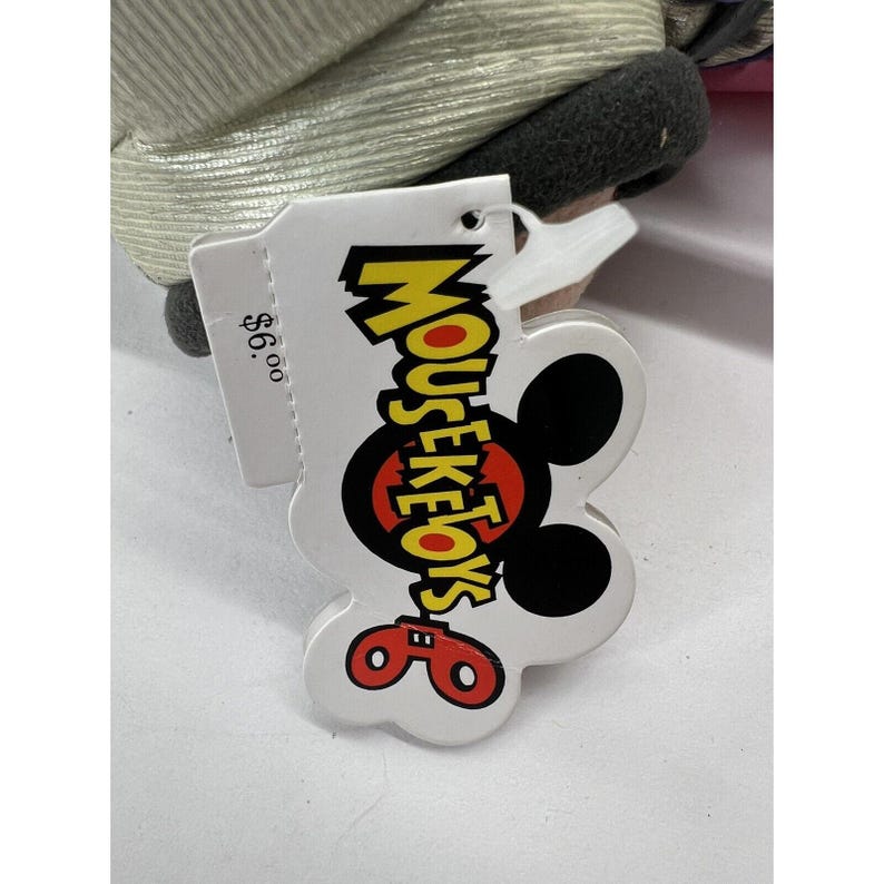 May include: A white tag with a black Mickey Mouse head and the text "Mouseketoys" in yellow letters. The tag also has a red price tag that says "$6.00".