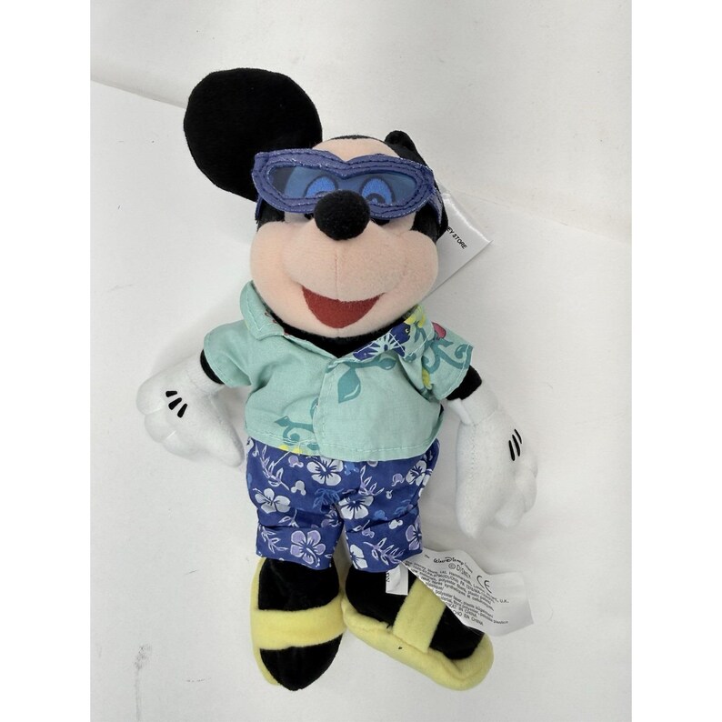 May include: A Mickey Mouse plush toy wearing sunglasses, a light green shirt with floral accents, and blue floral print shorts. The toy has black ears, a black nose, and yellow and black sandals.