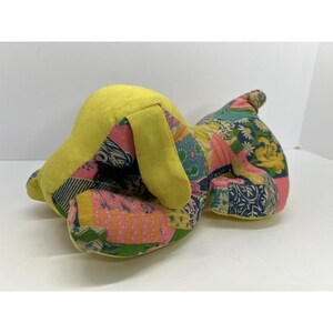 May include: A yellow patchwork dog toy with a pink, green, and blue floral pattern. The dog is lying down with its head resting on its paws.