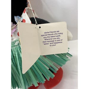Puede incluir: Mu&ntilde;eca de peluche con cabeza negra, pelaje blanco y falda roja y verde. La mu&ntilde;eca tiene una etiqueta que dice "Aloha Friends are special friends who bring you the island spirit."