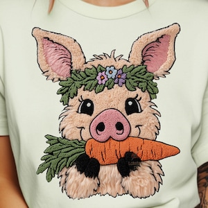 Könnte beinhalten: Hellgrünes T-Shirt mit einem gestickten Schweinedesign. Das Schwein trägt einen Blumenkranz und hält eine Karotte. Das Schwein hat rosa Ohren und eine rosa Nase. Das Design ist auf dem T-Shirt zentriert.