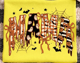 May include: A yellow t-shirt with the word "MAMA" in a Halloween-themed design. The letters are decorated with pumpkins, ghosts, bats, and spiderwebs. The shirt has a relaxed fit and is perfect for the spooky season.