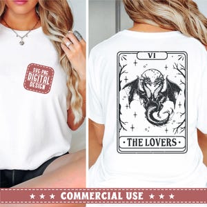 May include: A white t-shirt with a black and white illustration of a tarot card depicting two dragons intertwined. The card is labeled "VI - THE LOVERS".
