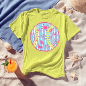 May include: A yellow t-shirt featuring a circular design with a pink sun, waves, and tropical elements like flowers, seashells, and a surfboard. The design is set against a blue and white striped background, evoking a beach theme.