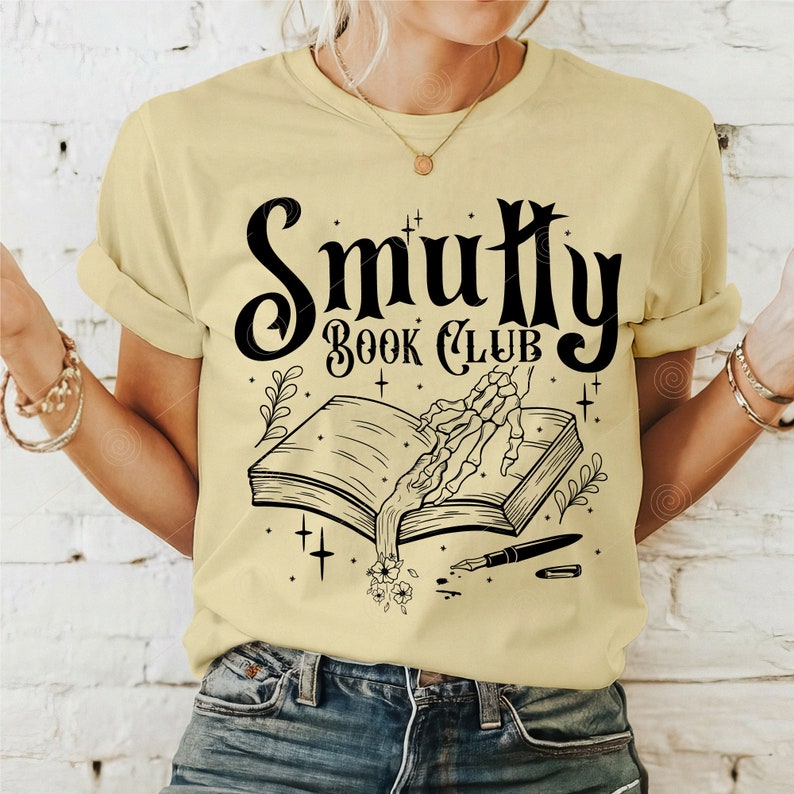 May include: A yellow t-shirt with the text "Smutty Book Club" in black. A black and white illustration of a skeleton hand reaching into an open book with a quill pen and flowers.