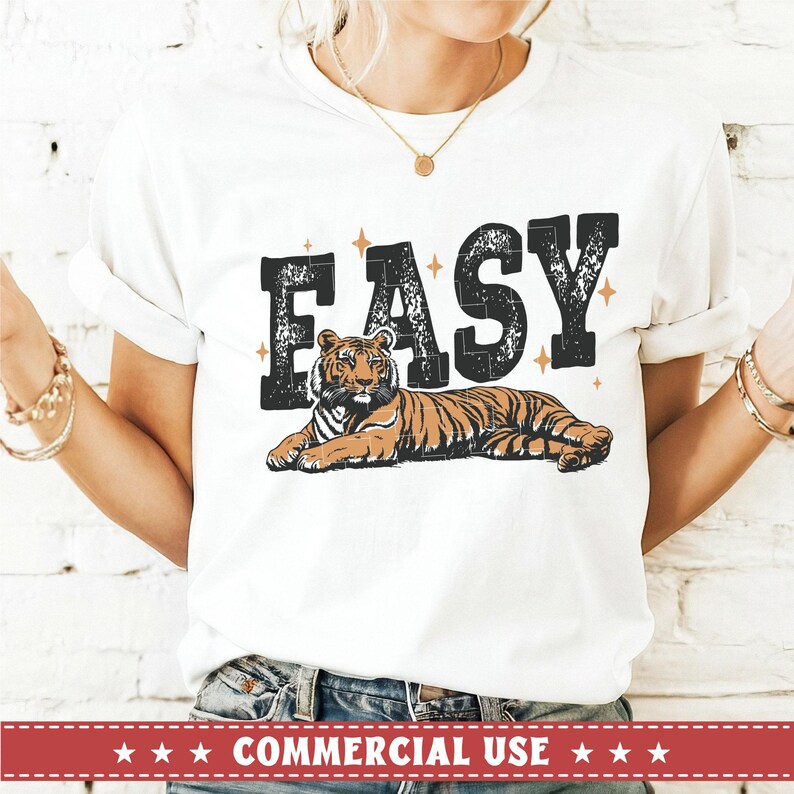 May include: White t-shirt with the word "EASY" printed in black with a distressed look. A tiger is lying down below the word.