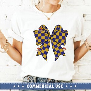 以下が含まれることがあります： 前面に黄色と青のチェック柄のリボンが付いた白いTシャツ。リボンはほつれた縁取りがあり、結び目があります。カジュアルなスタイルに最適なTシャツです。