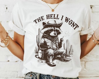 May include: White t-shirt featuring a graphic of a raccoon wearing a cowboy hat and sunglasses. The raccoon is sitting on a cactus and smoking a cigarette. The text "THE HELL I WONT" is printed above the raccoon.