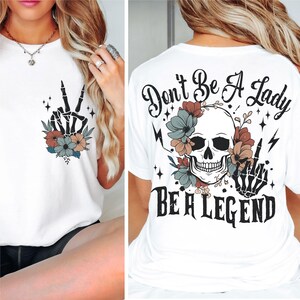 May include: White t-shirt with a skull and flowers graphic on the back. The text "Don't Be A Lady Be A Legend" is printed below the graphic. The front of the shirt has a peace sign with flowers.