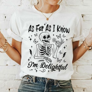 May include: White t-shirt with a black skeleton graphic holding a flower and butterflies. The text "As Far As I Know I'm Delightful" is printed on the shirt.