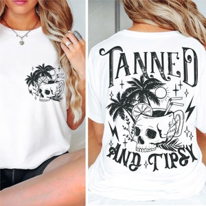 May include: White t-shirt with a black and white graphic of a skull in a cocktail glass with palm trees and the text "Tanned and Tipsy".