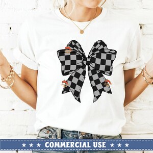 以下が含まれることがあります： 白地に黒と白のチェック柄のリボンがデザインされたTシャツ。リボンは大きく、ほつれた縁があります。