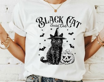 May include: White t-shirt featuring a black cat wearing a witch hat, a jack-o'-lantern, bats, and stars. The text "BLACK CAT Social Club" is printed above the cat. The design is a Halloween theme.