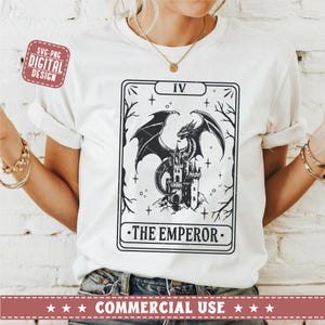 May include: A white t-shirt with a black and white illustration of a tarot card. The card depicts a dragon perched on a castle with the Roman numeral IV and the text "THE EMPEROR".