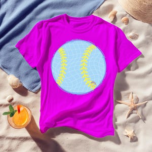 May include: A magenta t-shirt featuring a large baseball graphic. The baseball design is light blue with yellow stitching. The shirt is made of a soft material and is suitable for casual wear.