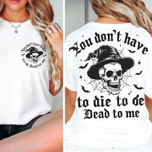 May include: White t-shirt with a black graphic of a skull wearing a witch hat, surrounded by a spiderweb and bats. The text "You don't have to die to be Dead to me" is printed on the front and back.