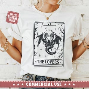 May include: A white t-shirt with a black and white illustration of a tarot card. The card is the Lovers card, which is number VI in the Major Arcana. The card features a two-headed dragon with wings spread out.