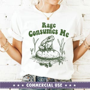 May include: White t-shirt with green text that reads "Rage Consumes Me" and a green illustration of a frog sitting on a rock in a pond.
