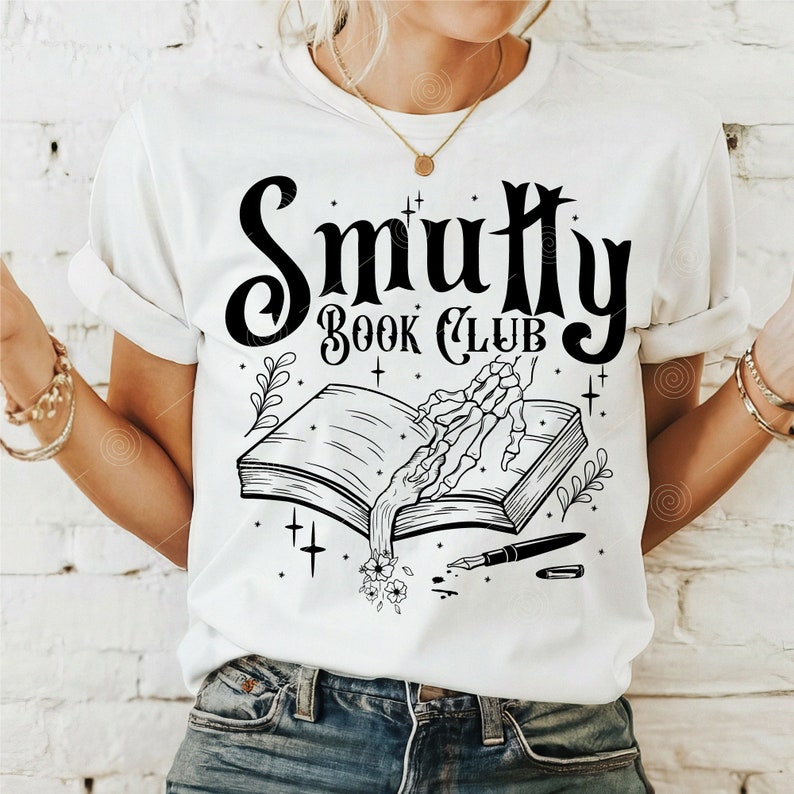 May include: White t-shirt with a black graphic design that says "Smutty Book Club". The graphic features a skeletal hand reaching for an open book with flowers growing from the pages.