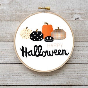 May include: A white embroidery hoop with a cross-stitch design of four pumpkins and the text "Happy Halloween". The pumpkins are orange, black and white polka dot, and black and white plaid.